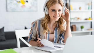 Selective focus of attractive woman in headphones looking at laptop while studying online